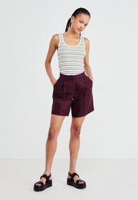 Striped tank top in white and black, paired with plum-colored shorts featuring a button, pleats, and side pockets. Black platform sandals.