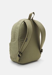 Zaino imbottito verde oliva con spallacci regolabili, una maniglia superiore e un piccolo logo nero del marchio su una delle cinghie.