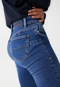 Jeans i mellanblå denim med en tajt passform, som har en märkeslogotyp vid midjan, bakfickor med texturerad sömnad och slät tyg.