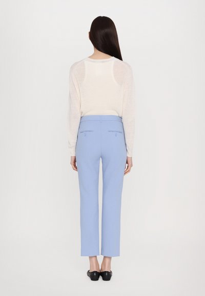 Lightweight, cream knit sweater with long sleeves paired with high-waisted, straight-leg trousers in light blue, featuring back pockets.