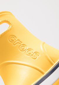 Klart gula Crocs med en texturerad yta och framträdande logotyp. Designen inkluderar ett cirkulärt utskärning för andningsförmåga och komfort.