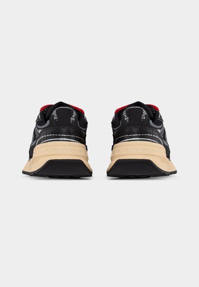 Paire de baskets noires et beiges avec doublure intérieure rouge, vues de dos sur fond blanc.