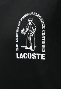 Εικονογράφηση τενίστα σε λευκό με το κείμενο «Ο θρύλος της γαλλικής κομψότητας συνεχίζεται» και «Lacoste» σε μαύρο υφασμάτινο φόντο.