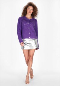 Lila kötött kardigán díszes gyöngyökkel az elején, kerek nyakkivágással, gombos záródással és hosszú ujjal.