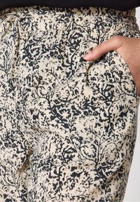 Lichte katoenen broek met een elastische tailleband, voorzien van een zwart bloemenpatroon op een beige achtergrond, en zijzakken.
