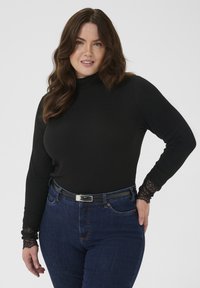 Maglione a collo alto nero a costine con pizzo ai polsini, abbinato a jeans blu a vita alta e una cintura nera con fibbia argentata.