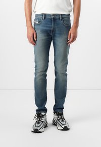 Slim fit, elhalványult kék farmernadrág öt zsebbel, kontrasztos varrással és klasszikus gombos zárással, fekete és ezüst sportcipővel párosítva.