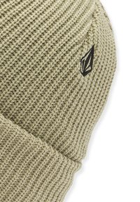 Strikket beanie i lys olivengrøn med et tekstureret mønster. Har et sort logo-mærke på siden. Blødt, strækbart materiale.