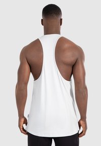Weißes Tanktop mit Racerback-Design, aus weichem Baumwollmaterial und lockerer Passform, das die Rückenpartie und die freiliegenden Arme zeigt.