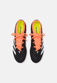 Scarpe da calcio nere in materiale testurizzato, con lacci arancioni brillanti e un'insole giallo neon, decorate con tre strisce bianche.