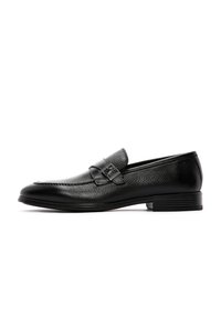 Zwarte leren loafers met een gestructureerde afwerking, voorzien van een band met een gespsierraad, lage hak en afgeronde neus.