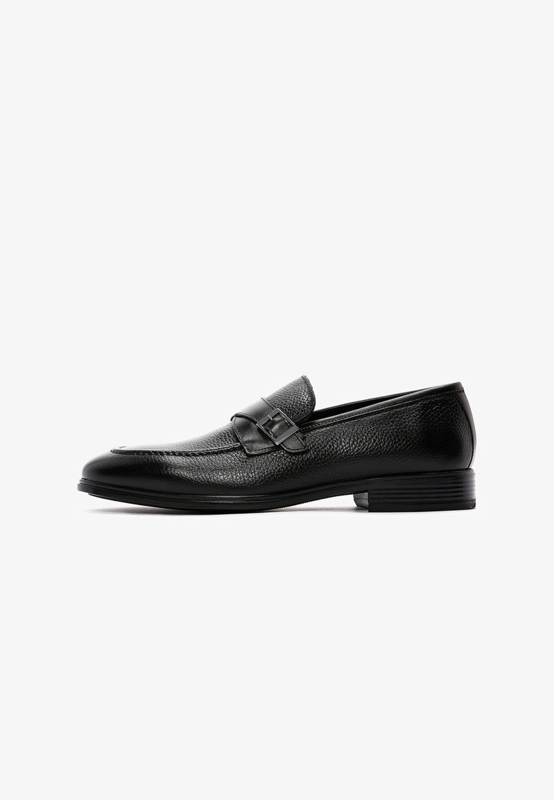 Zwarte leren loafers met een gestructureerde afwerking, voorzien van een band met een gespsierraad, lage hak en afgeronde neus.
