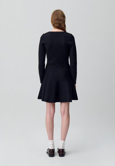 Abito nero a maniche lunghe con corpino aderente e gonna svasata. Tessuto liscio con dettagli di design minimi, presenta accenti sulle spalle e un taglio classico.