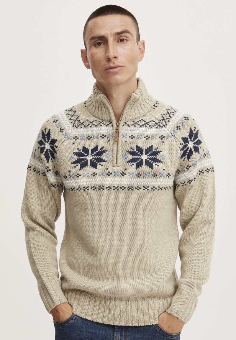Beige neulepullover, jossa on korkea kaulus. Rinnassa on sinisiä ja tummansinisiä lumihiutaleita sekä ribbikujetteet hihansuissa ja helmassa.