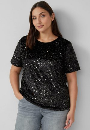 Schwarzes Paillettentop mit kurzen Ärmeln und rundem Ausschnitt, das eine weiche Textur und ein glänzendes Oberflächendetail aufweist. Kombiniert mit hellgrauen Jeans.