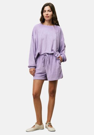 Ensemble de vêtements de détente lilas comprenant un haut à manches longues au fit décontracté et un short à cordon de serrage. Texture douce, branding minimal et tissu léger.