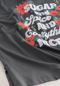 Fekete póló fehér „Sugar and Spice and Everything Nice” felirattal; piros mikulásvirágokkal és zöld levelekkel díszítve, sima pamut anyagból.