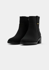 Botas pretas até ao tornozelo feitas de imitação de couro texturizada, com fecho lateral e um detalhe em dourado, apresentando um pequeno salto quadrado. Design suave de biqueira arredondada.