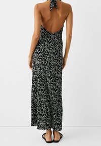 Czarna maxi sukienka w kwiatowy wzór z dekoltem halter, otwartymi plecami i zwiewnym materiałem. Noszona z płaskimi czarnymi sandałami.