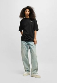 Black oversized t-shirt with short sleeves, featuring white text detail, paired with light blue baggy jeans and white sneakers.