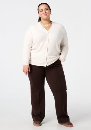 Lichtbeige cardigan met gestructureerde bolletjes, knopen aan de voorkant, gecombineerd met donkerbruine broek. Zacht materiaal en een ontspannen pasvorm.