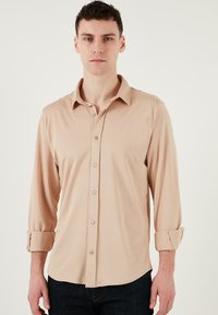 Beige hosszú ujjú gombos ing, standard gallérral és felgöngyölt ujjakkal, sima textúrával és illő gombokkal.