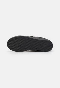 Sole di sneakers nera con un design testurizzato caratterizzato da un motivo a nido d'ape. La base in gomma si raccorda dolcemente con una leggera curvatura.