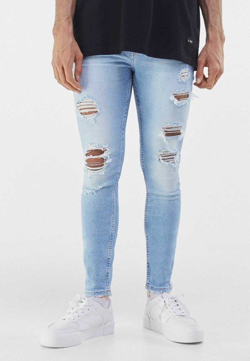 Ljusblå tajta jeans med slitna hål och fransiga kanter. Kombinerade med vita sneakers med slät läderstruktur.