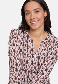 Blusa a maniche lunghe in tessuto leggero con un motivo astratto nei colori rosa, marrone e crema, caratterizzata da scollatura a V e dettagli di cucitura decorativa.