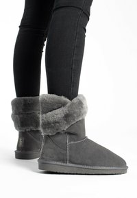 Botines de ante gris con un grueso puño de piel sintética gris, suela plana y detalles de costura reforzada visibles en el diseño.