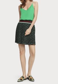 Vihreä satiinihihna-yöpaita, mustat skortit kukkakuviolla ja vihreät liukuva kengät, joissa on palmun kuvioita.