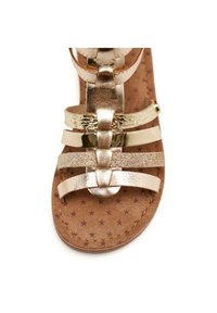 Gouden metallic sandalen met banden, met een platte zool, geweven banden en een bruine voetbed met sterpatronen. Versterkt met een veilige gesp.