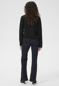 Svart långärmad topp med en figurnära midja, parat med mörkblå utsvängda jeans. Båda materialen ser släta ut med minimal detaljering.