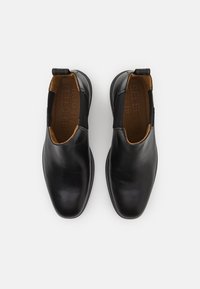 Zapatos de cuero negro con punta afilada y paneles laterales elásticos. Textura suave con un brillo sutil. Además, cuenta con una lengüeta para facilitar su uso.