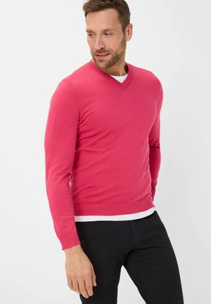 V-neck sweater in vibrant pink, made of soft material. Fitted design with ribbed cuffs and hem. Worn over a white t-shirt and black pants.