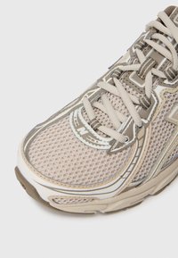 Beige sportschoen met bovenwerk van mesh, textuuraccenten en grijze details. Heeft een ronde neus, vetersluiting en rubberen zool.