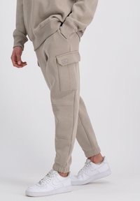 Bežové cargo nohavice z mäkkej tkaniny, s bočnými vreckami, zúženými členkami a voľným strihom. V kombinácii s bielymi teniskami.