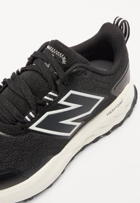 Baskets noires avec un dessus en textile, arborant un logo "N" blanc, des détails texturés et une semelle de couleur claire contrastante.