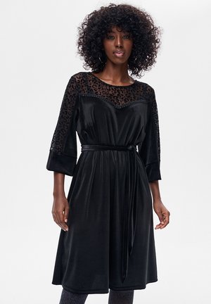 Czarna sukienka z przezroczystym karczkiem w panterkę, rękawami 3/4 i paskiem w talii. Wykonana z miękkiej tkaniny o gładkiej fakturze. Długość sięga do połowy łydki.