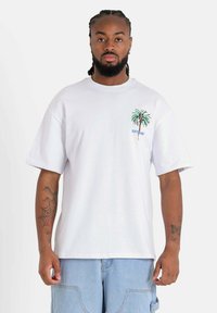 Witte oversized t-shirt met een palmboom graphic op de linkerkant van de borst en de tekst "SIXTYTUNE" in het blauw. Katoenen stof, korte mouwen.