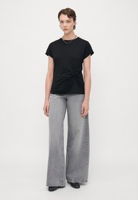 Svart kortärmad t-shirt med en knuten detalj framtill, ihop med högmidjade grå jeans med vida ben och svarta utsmyckade skor.