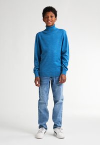 Blauer Rollkragenpullover aus strukturiertem Strick, kombiniert mit hellblauen Jeans und weißen Sneakers. Der Schnitt ist lässig mit langen Ärmeln.
