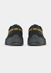 Par de zapatos deportivos negros y amarillos vistos desde atrás sobre un fondo blanco liso.