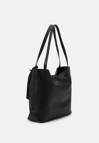 Czarna skórzana torba na ramię z dwoma paskami. Charakteryzuje się gładką teksturą i szczegółem w postaci frędzla z boku. Otwarta góra zapewniająca łatwy dostęp.