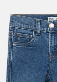 Μπλε τζιν παντελόνι με μπροστινή τσέπη, θηλιές για ζώνη και κλείσιμο με μεταλλικό κουμπί, με ετικέτα μάρκας στ ο εσωτερικό της μέσης.