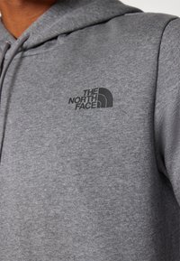 Grå hættetrøje lavet af blødt stof med et sort logo af "The North Face" på venstre brystområde. Simpelt design med en afslappet pasform.