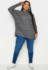 Överdimensionerad grå långärmad topp med en melerad textur, i kombination med figursydda blåjeans och vita sneakers. Enkelt, avslappnat outfit.