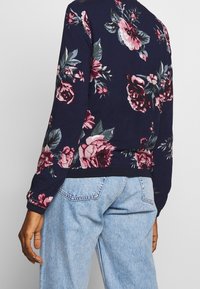 Navy sweatshirt med blommönster, lång ärm, rund hals, ribbade cuffs och nederkant. Kombinerad med ljusblå denimjeans.