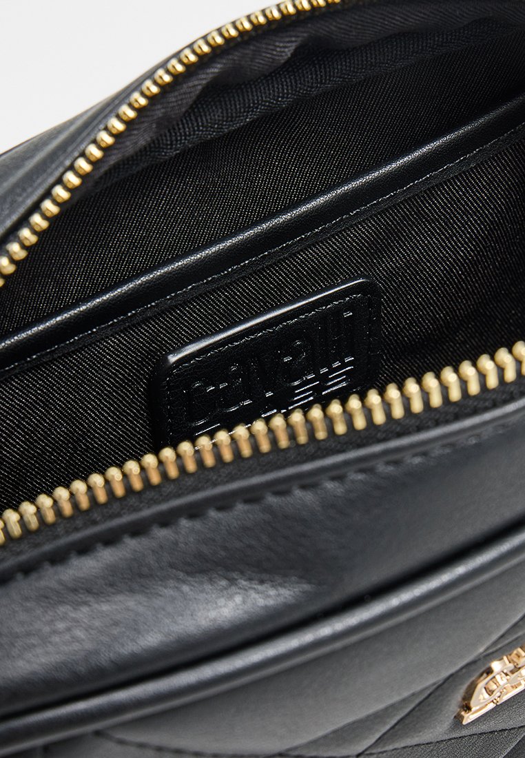 Interior de un bolso de mano de cuero negro con cierre de cremallera, con textura suave, forrado en tela negra y con una etiqueta de la marca presente.