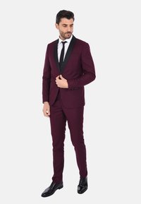 Completo bordeaux con rever in raso nero, pantaloni slim fit, camicia bianca e cravatta nera, completato con eleganti scarpe nere lucide.